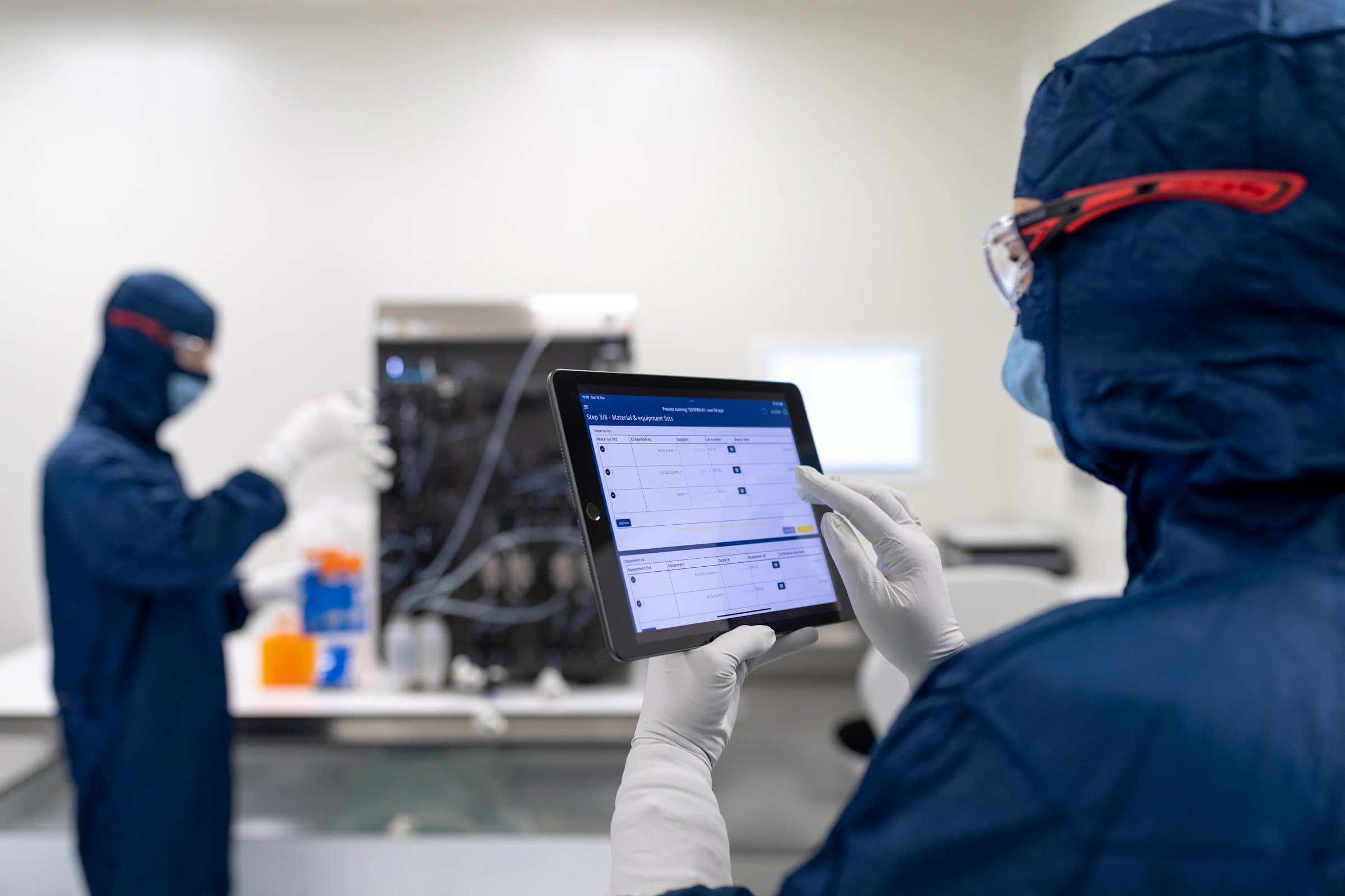 Profissional com uniforme de área limpa acompanhando a produção em um tablet